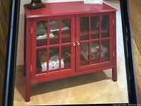 Front view of red painted wooden cabinet with two glass pane doors and silver knobs, showing clear condition and structural details.