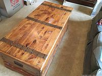 Top side view showing cedar wood surface with three brass accent straps and rivets, handles on side visible.