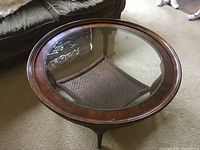 Top angled view showing the round wood frame with glass insert and rattan shelf below.