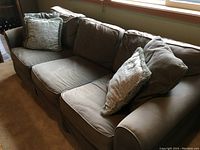 Faded green fabric couch with three cushions and two decorative pillows, side view.