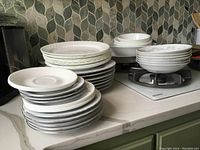 Stacked white dishes including plates, bowls, and saucers on a kitchen counter.