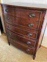 Front view showing the curved drawer fronts of the vintage wooden highboy dresser with 5 drawers and oval metal pulls.