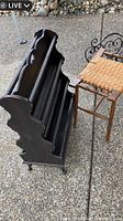 Dark wood magazine rack with carved sides and three shelves next to the rattan stool.