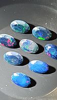 Seven oval faceted Ethiopian black opal gemstones with visible multicolor flashes including blue, green, red, and purple.