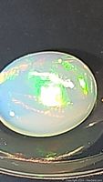 Close-up photo showing the oval cabochon Ethiopian opal with bright green and yellow flashes on semi-translucent white base.