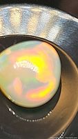 Close-up of the teardrop-shaped opal gemstone showing vibrant internal rainbow colors and smooth cabochon cut surface.