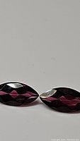 Close-up photo of two marquis cut faceted Rhodolite garnet gemstones showing their deep pink color and cut facets.