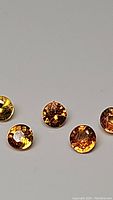 Photo showing a close-up of multiple small round cut sapphires with vibrant yellow to orange coloration and faceted cuts.