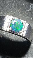 Close-up photo showing the vibrant Ethiopian black opal with its play-of-color in green and blue hues set in a silver band.