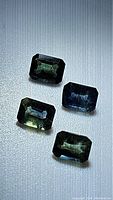 Four emerald cut blue green sapphires arranged on a textured light background to show faceting and color.