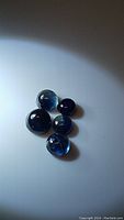 Five round blue sapphire cabochons in mixed sizes and shades under white light showing inclusions and surface reflectance.