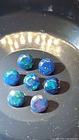Close-up photo showing eight calibrated round cut black opals with multicolor flashes on a black dish