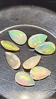 Close-up photo of 8 pear cut Ethiopian opal stones arranged in a circular pattern, showing rainbow color flashes and translucency.