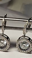 Close-up of certified Moissanite earrings showing the 5mm center stones and halo of CZ accents, rhodium plated sterling silver metal.