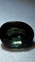 Close-up photo of deep green oval sapphire showing facets and color variations with deep forest green and blue undertones.