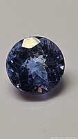 Close-up of the round diamond cut blue-purple tanzanite gemstone showing the top facet and internal reflections