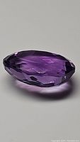 Side angle view of the oval cut natural amethyst showing the elongated faceted shape and deep purple color.