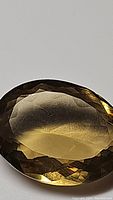 Oval cut natural champagne colored citrine with visible facets and warm golden hue, photographed on a plain surface to highlight clarity and color.