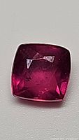 Top view of cushion cut natural ruby showing deep pink red color and visible inclusions.