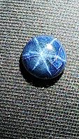 Close-up photo of natural blue star sapphire cabochon showing clear six-ray star asterism and surface inclusions.