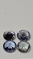 Close-up of four natural tanzanite stones showing dome-shaped cabochon and diamond cut facets with blue-violet hues.