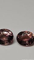 Two oval-cut Padparadscha color tourmaline gemstones photographed on a plain background to highlight color and clarity.
