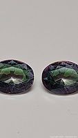 Close-up of two oval cut mystic topaz gemstones with visible rainbow colors and faceting.