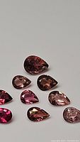 Multiple small loose pink tourmaline gemstones arranged on a flat surface showing pear and oval faceted cuts in various shades of pink and red.