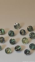 Photo displaying multiple round-cut Alexandrite gemstones with visible color variation under different lighting conditions.
