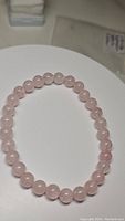 Photo of the bracelet showing natural soft pink rose quartz beads arranged in a circle on a white surface.