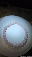 Photo of natural rose quartz bead bracelet lit from above, showing smooth spherical beads with light pink color.