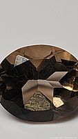 Close-up photo of the natural oval cut smokey quartz gemstone showing facets and color in detail.
