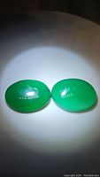 Pair of vivid green oval cabochon onyx stones under bright light showing translucent glossy finish.