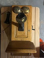 Top view of the antique wooden wall phone showing brass bells and mouthpiece horn, with black handset placed on the left.