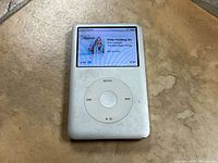 Front view of Apple iPod Classic showing screen with song playing.