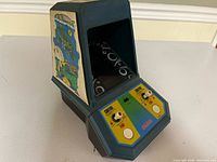 Left angled view of the Coleco Galaxian mini arcade game showing side artwork and control panel with toggle switches and buttons.
