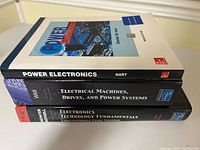 Stack of three textbooks titled 'Power Electronics', 'Electrical Machines, Drives, and Power Systems', and 'Electronics Technology Fundamentals'.