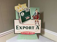 Full view of the three-dimensional cardboard cigarette advertisement displaying MacDonald's Export 'A' Filter Tip Virginia Cigarettes with some water damage.