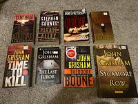 Top-down view of eight fiction paperback books arranged in two rows on carpeted floor.
