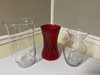 Three glass vases displayed on floor corner wall, showing full shapes and color