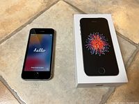 iPhone SE (2016) front displaying 'hello' setup screen next to box with front cover image