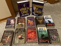 Photo showing the full collection of 11 Jack Whyte books arranged on carpet, mostly standing or lying flat, showcasing titles and cover art.