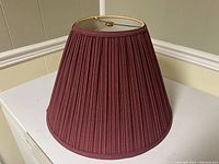 Front angled view of the pleated burgundy fabric lamp shade sitting on a white surface showing overall shape and fabric texture.