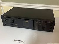 Front angled view of Nakamichi BX-100 cassette deck showing power button and cassette compartment door with tape transport buttons on left panel.