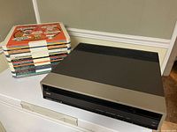 Front view showing RCA SelectaVision player with stack of plastic video disc sleeves behind