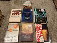 Seven books spread on carpet floor showing their front covers: Safe in the Shepherd's Arms, Brief Answers to the Big Questions, Chariots of the Gods?, The Second Messiah, The God Delusion, The End of the World, Nothing But the Truth