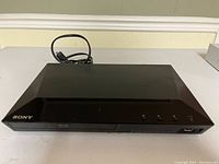 Front top view of the Sony BDP-S1100 Blu-Ray/DVD player showing the disc tray, buttons, and Sony logo.