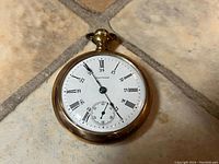 Front view of the pocket watch showing white dial with Roman numerals and sub-seconds dial. Visible hairline cracks on enamel face.