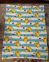 Full view of the blanket showing blue and white stripes with multiple Pikachu and Pokeball images.