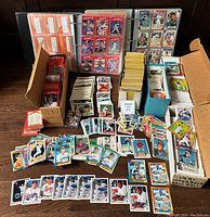 Overview of baseball cards in binders, boxes, and stacks, showing many cards spread on table with notable 1990 Donruss and Topps cards in binders